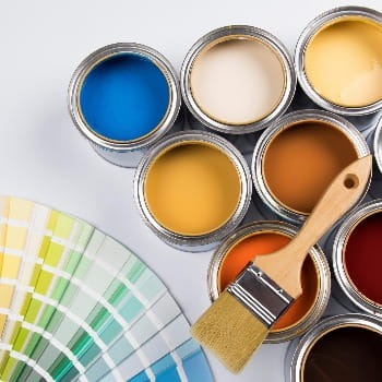 A paintbrush lying on top of eight open paint cans next to various swatches